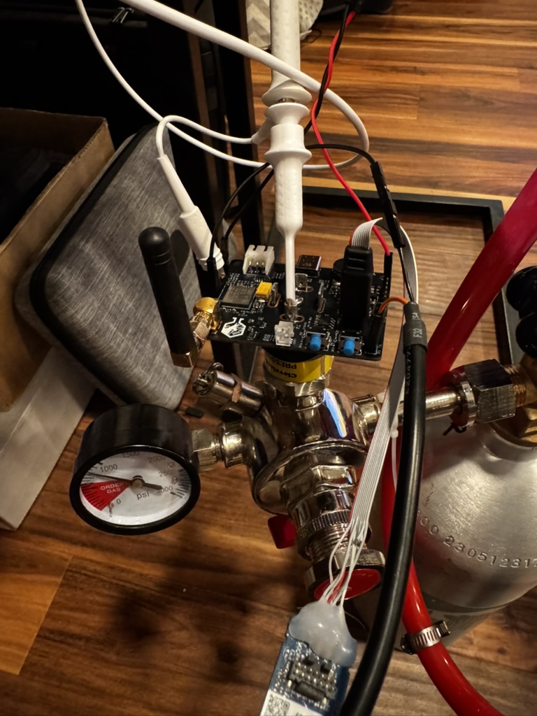 An exposed Barkeep sensor board with antenna, ribbon cable, and attached sensor breakout mounted on a chrome CO2 regulator and tank during hands-on refinement.