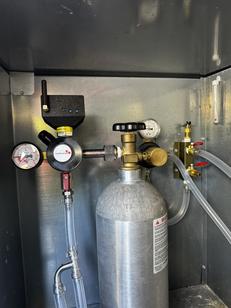 A Barkeep sensor installed in the field, monitoring a CO2 regulator and tank with pressure gauges and beverage lines inside a metal cabinet.