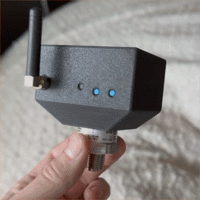 A hand holding a production Barkeep sensor with its antenna and threaded probe, status LEDs blinking as it powers up and pairs.